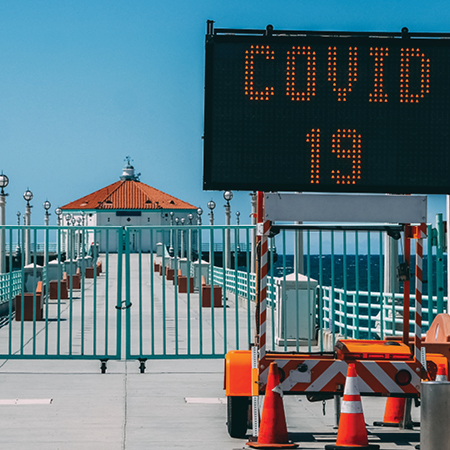 Gated boardwalk with ocean view and a COVID-19 sign.