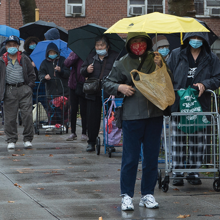 Group of people in masks in a line with umbrellas.