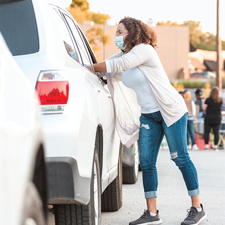 Woman wearing a mask reach into a car.