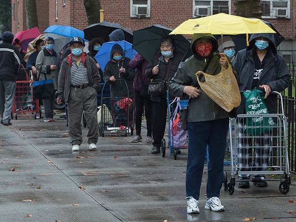 Group of people in masks in a line with umbrellas.