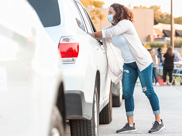 Woman wearing a mask reach into a car.