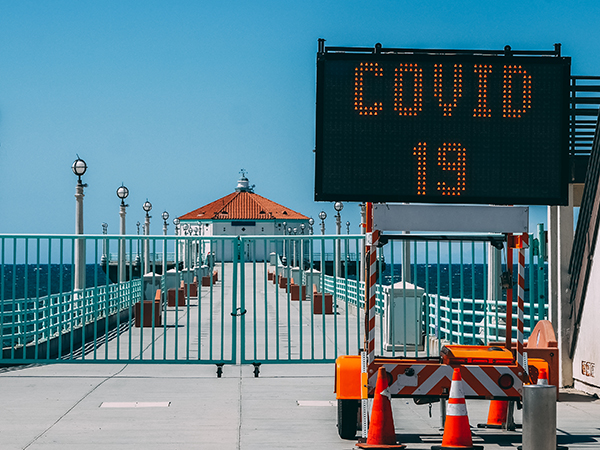 Gated boardwalk with ocean view and a COVID-19 sign.